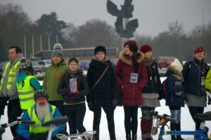 Zdjęcie dziesięciu osób tworzących górną-prawą część ustawionego na Jasnych błoniach WOŚP-owego serca . W dole widać kierownice i siodełka rowerów które tworzyły dolny zarys serca a nad nimi w centralnej części zdjęcia , uśmiechnięte postacie osób w różnokolorowych strojach . Po lewej stronie zdjęcia trzy osoby są ubrane w kamizelki odblaskowe NNT w tym jedna w kasku rowerowym i czerwonych o kularach . Inne osoby są w ubraniach wyjściowych z szalikami i w różnokolorowych czapkach oraz w strojach harcerskich z beretami na głowach . W centralnej części zdjęcia widać młode wolontariuszki WOŚP z zawieszonymi ma szyjach identyfikatorami i z puszkami w rękach . Dolną część tła tworzy biały śnieg a górną parking samochodowy nad którym widać rozmazane drzewa i Pomnik Czynu Polaków zwany popularnie Pomnikiem Trzech Orłów.